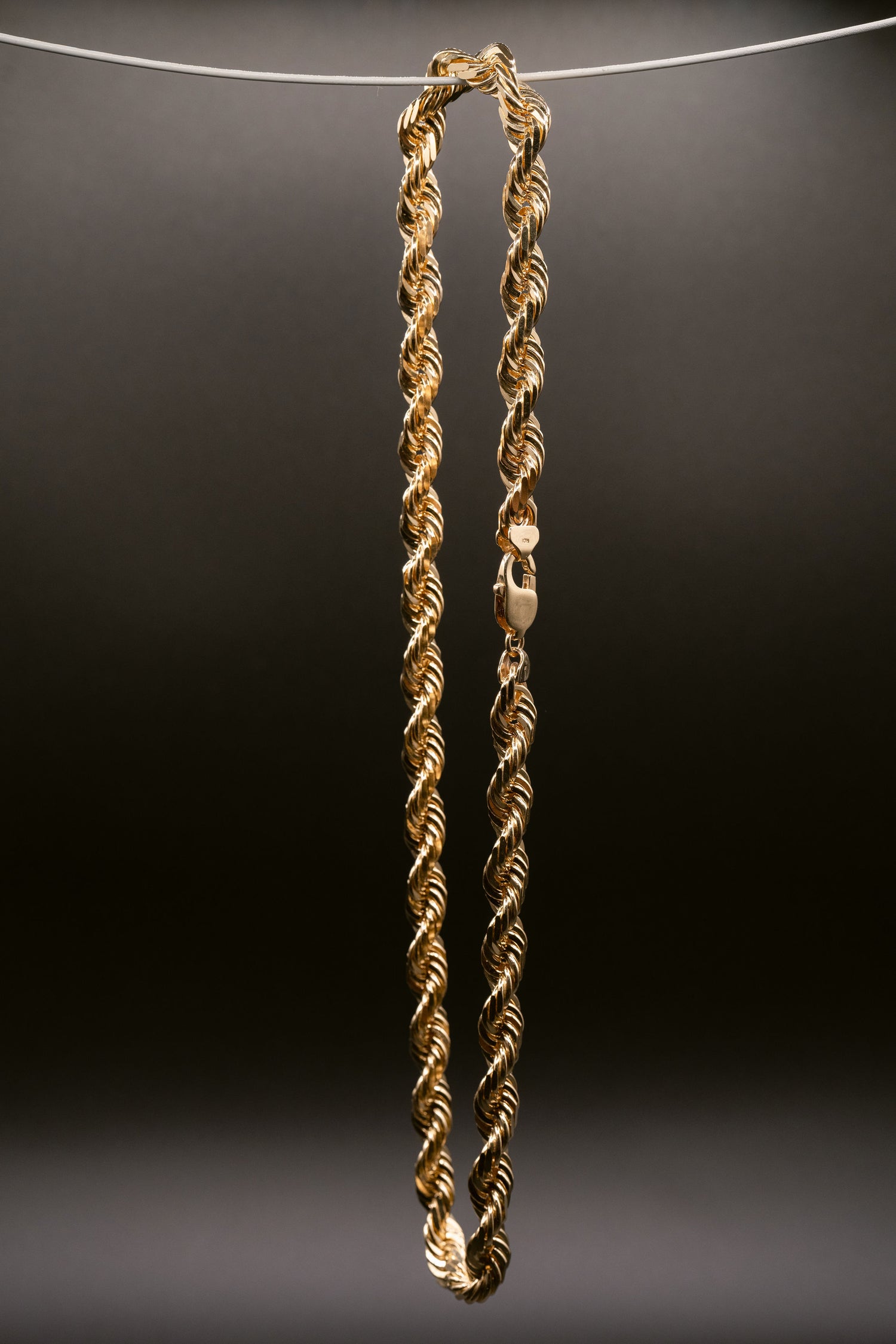 Single gold rope chain necklace suspended against a dark background, displaying its detailed and polished link design.