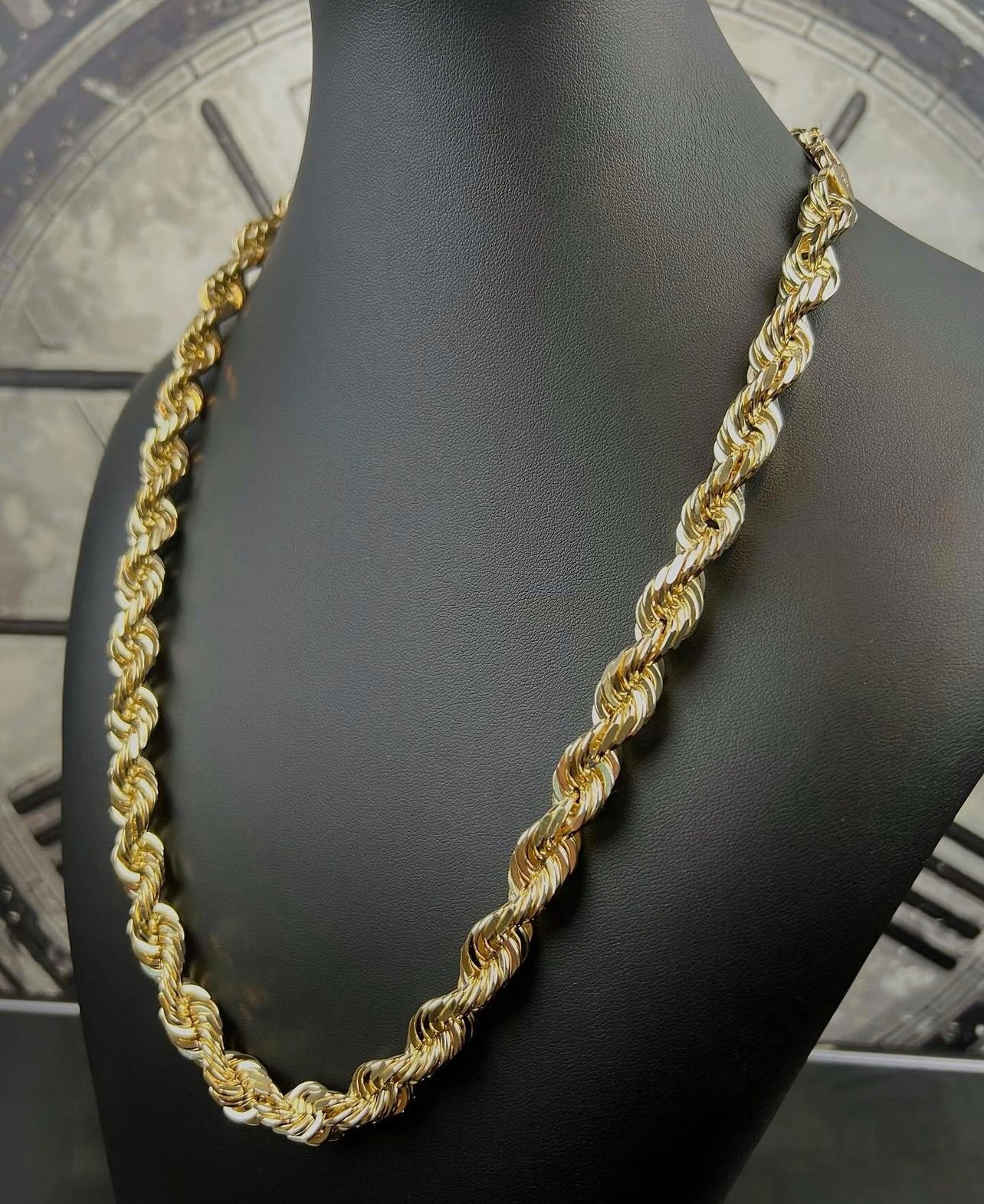 Close-up of a gold rope chain necklace displayed on a black mannequin, highlighting its intricate twisted links.